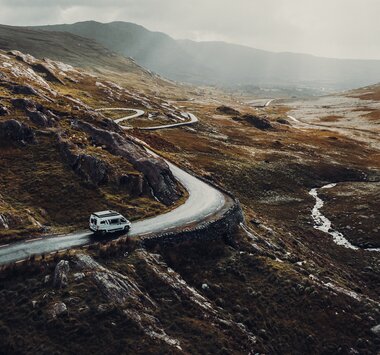 Carado motorhome on a winding mountain road through a vast, rocky hilly landscape, seen from above