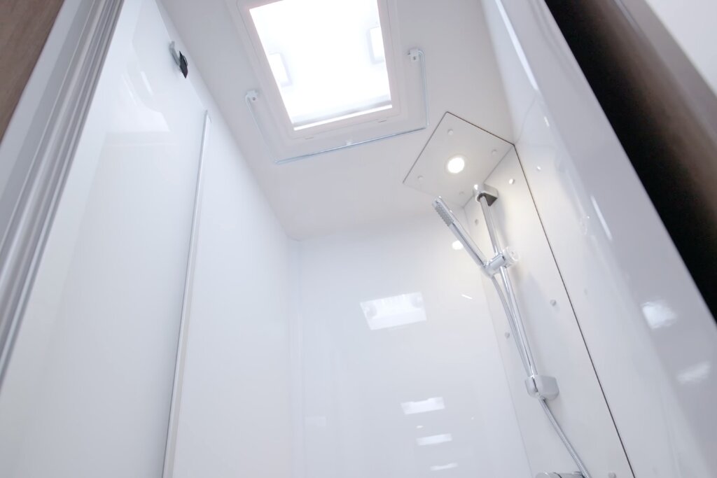 Shower compartment in a Carado motorhome with white wall paneling, handheld shower and roof window
