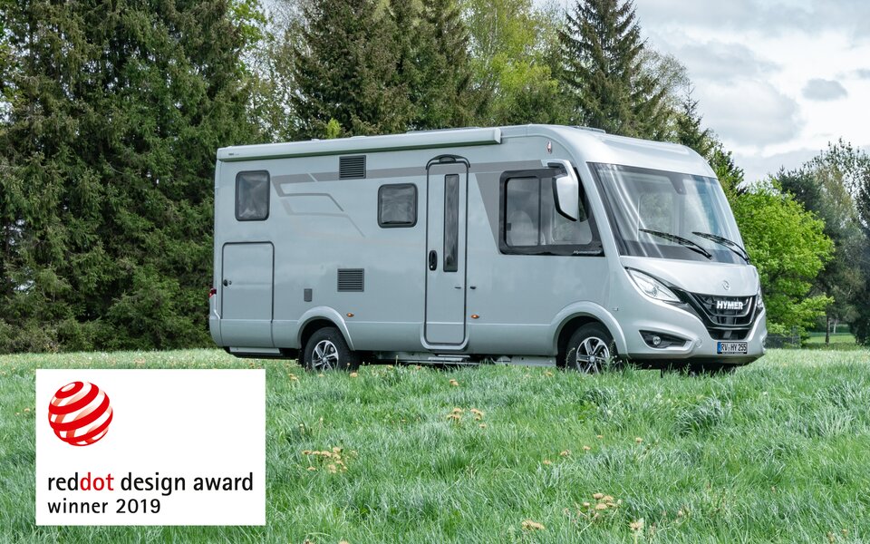 HYMER B-MC I WhiteLine standing on a meadow with trees in the background and emblem Reddot Design Award Winner 2019