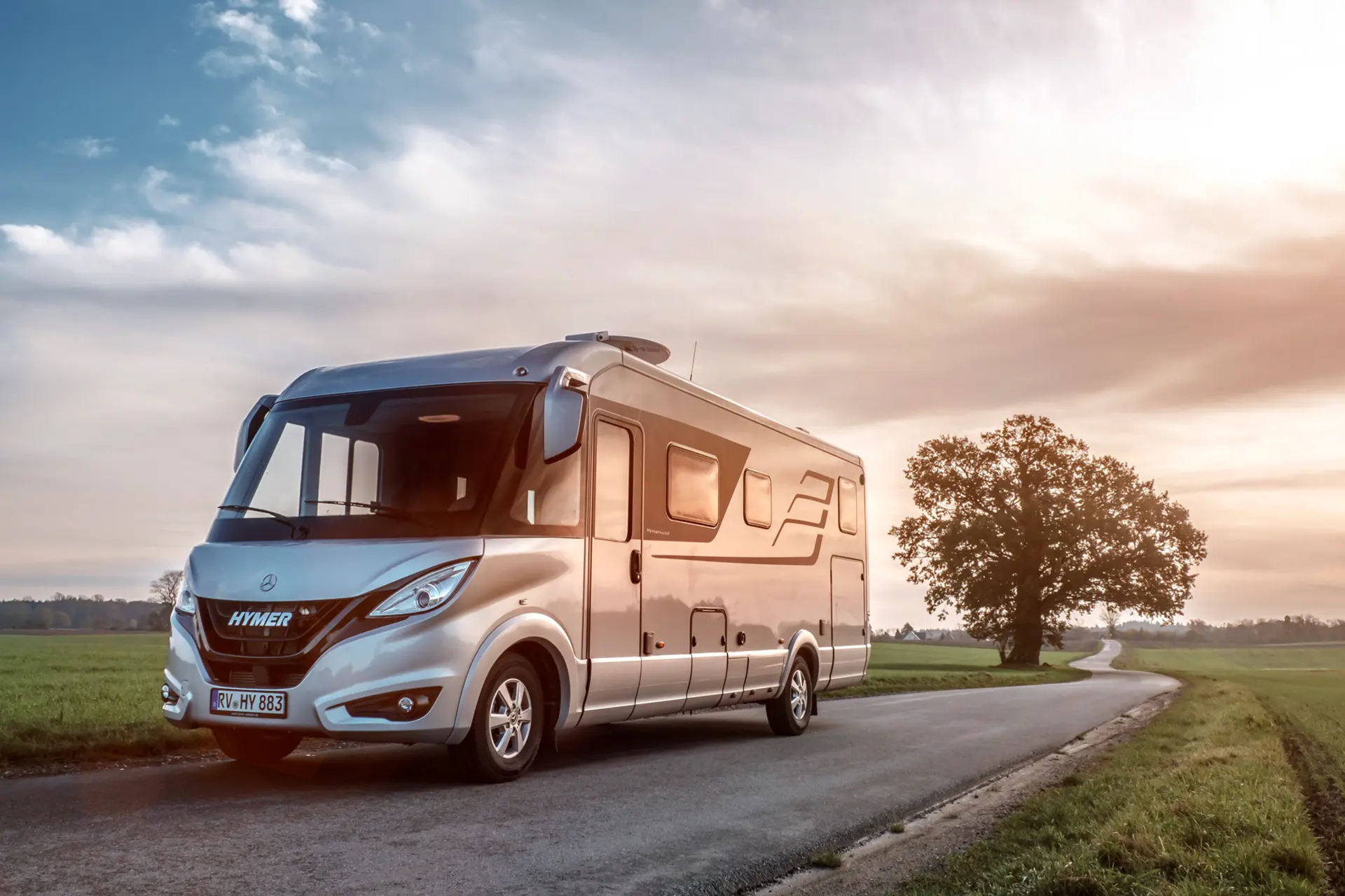 HYMER B-Class Masterline on the road in a flat landscape with green meadows and trees