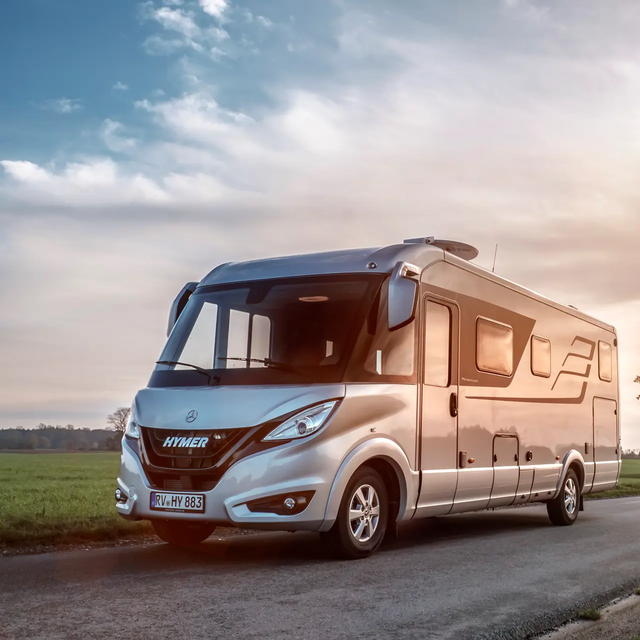 HYMER B-Klasse Masterline op de weg in een vlak landschap met groene weiden en bomen