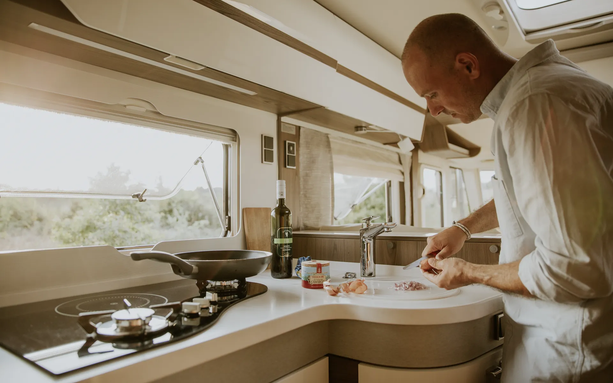 Man die uien hakt in de keuken van een camper - de pan staat op het gasfornuis