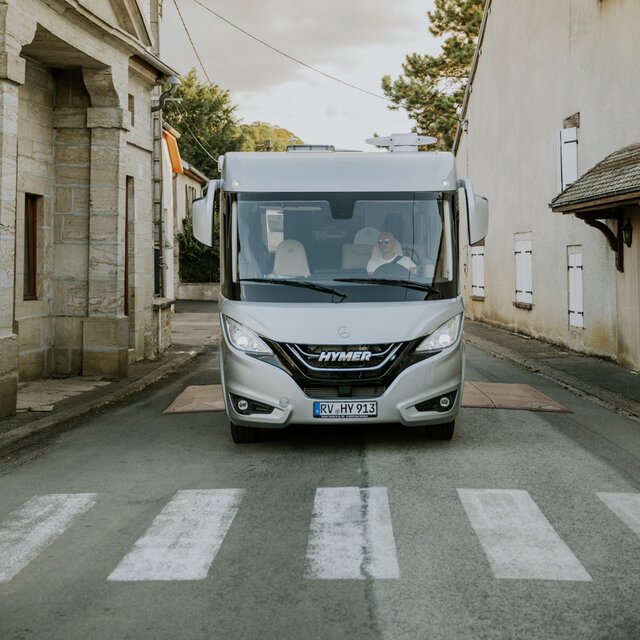 Vooraanzicht van een integraal HYMER camper B-ML I voor een zebrapad in een stad.