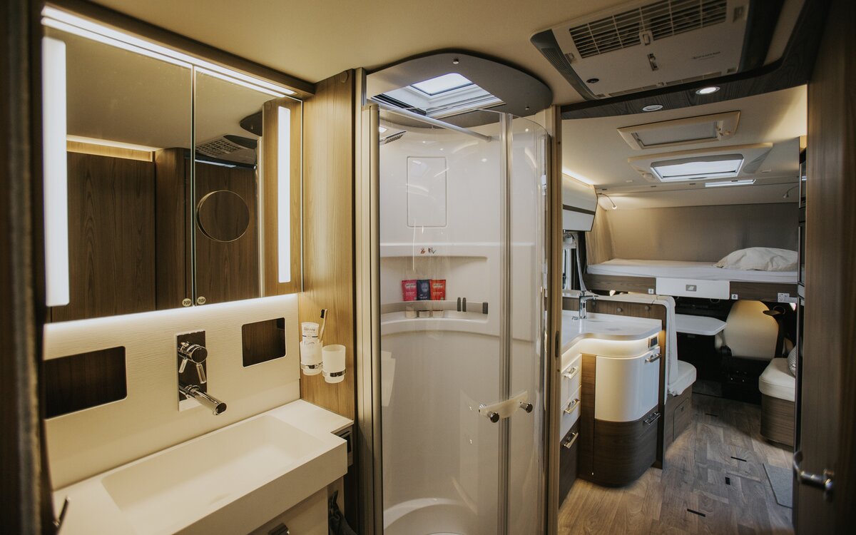 Interieur van een camper met grote badkamer in salon, aparte douche, keuken en hefbed op de achtergrond