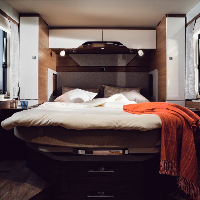 Queensize bed met crèmekleurig bedlinnen en rode sierdeken achterin de HYMER B-ML I 890
