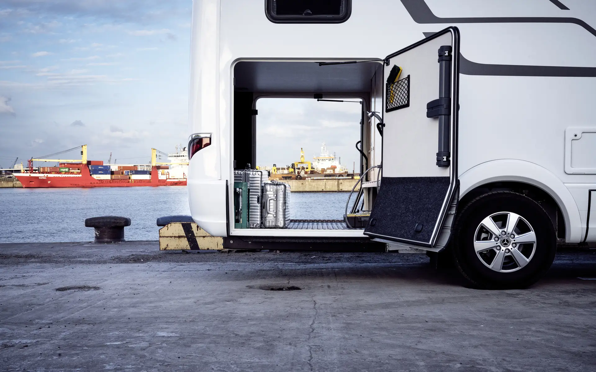 Uitzicht door de garage achter van de HYMER B-klasse MasterLine geladen met zilveren koffers voor de havenfaciliteit met het rode vrachtschip
