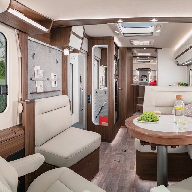 Woonkamer in de HYMER-B-MasterLine met een zithoek in crèmekleurige lederlook aan de set, ronde tafel