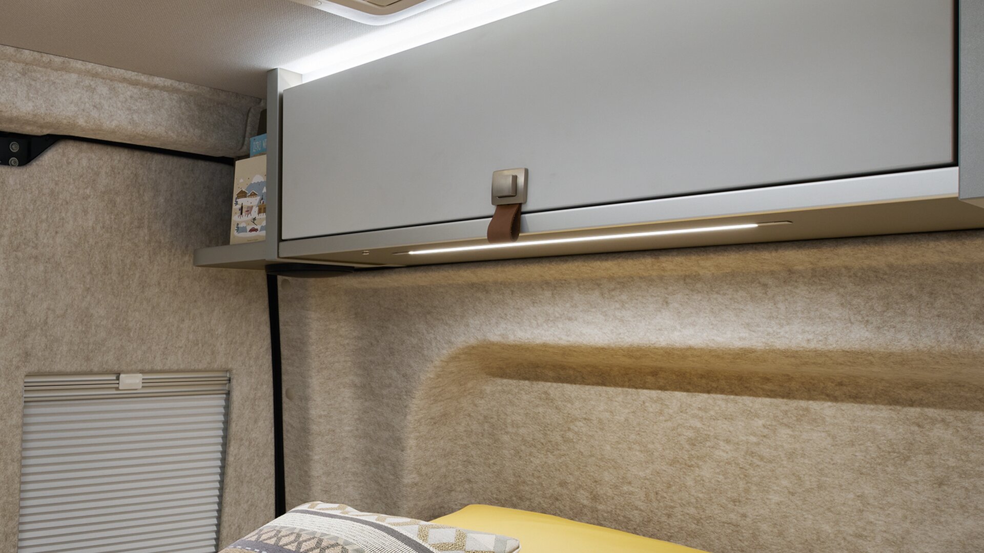 The walls of the HYMER Grand Canyon S in the Pearl Grey style world are covered with felt. The lighting above the roof storage cabinets is turned on.
