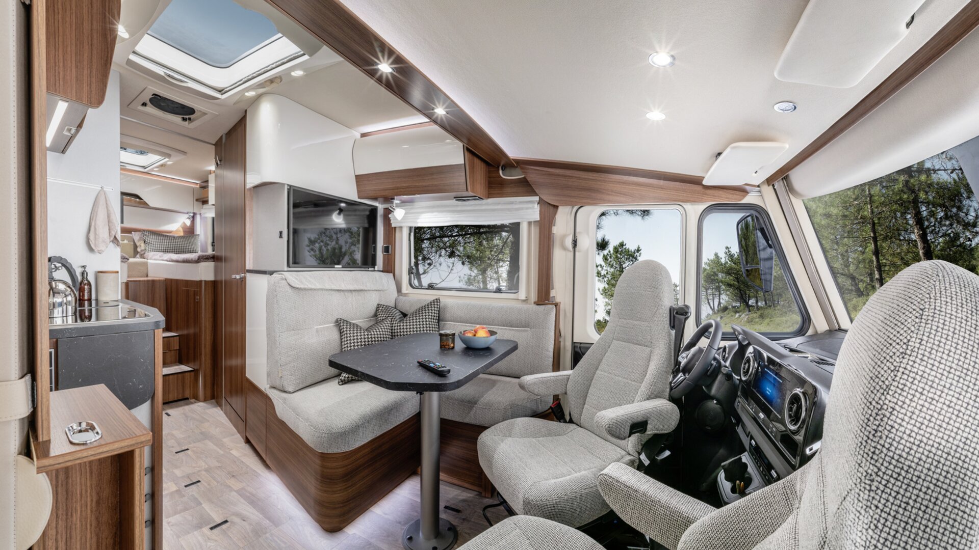 Lounge seating group with driver's seats and decorative cushions, TV plasma and kitchen in the HYMER B ModernComfort