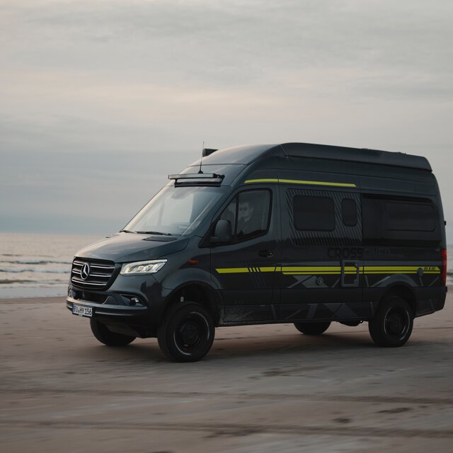 Black camper van with neon green special decals parked sideways at the beach, with the sea in the background