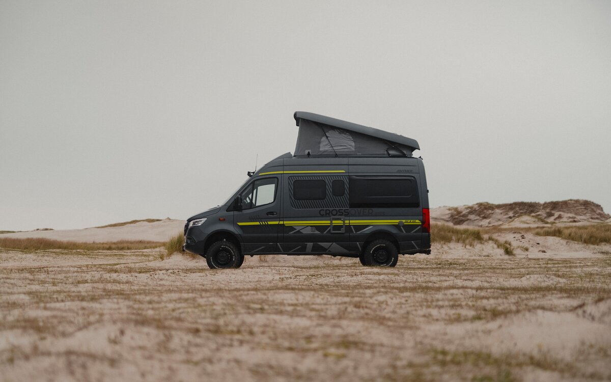 Black camper van with neon green special decals parked sideways in the sand, with dunes in the background, pop-up roof is open