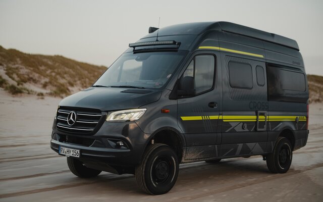 Black camper van with neon green special decals driving over sand, with dunes in the background