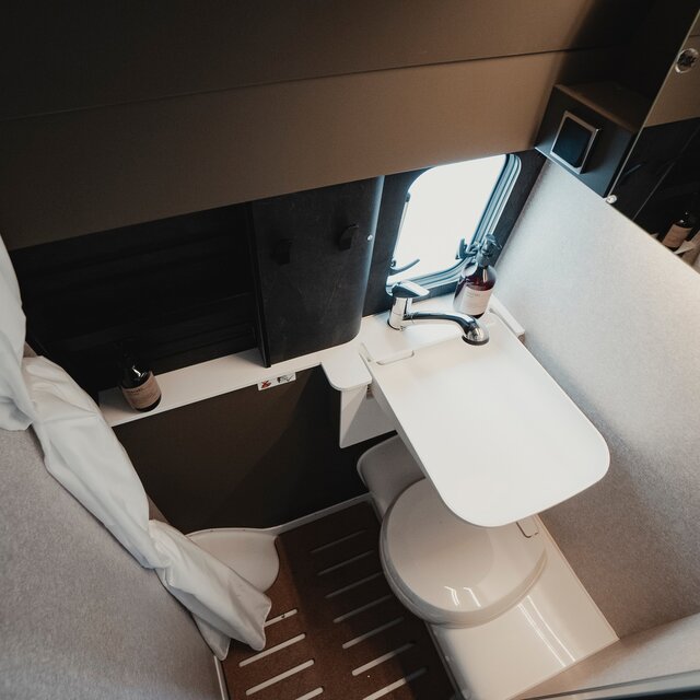 Bathroom in a camper van: shower cabin with sink, cassette toilet, mirror, storage cabinets, and shower curtain