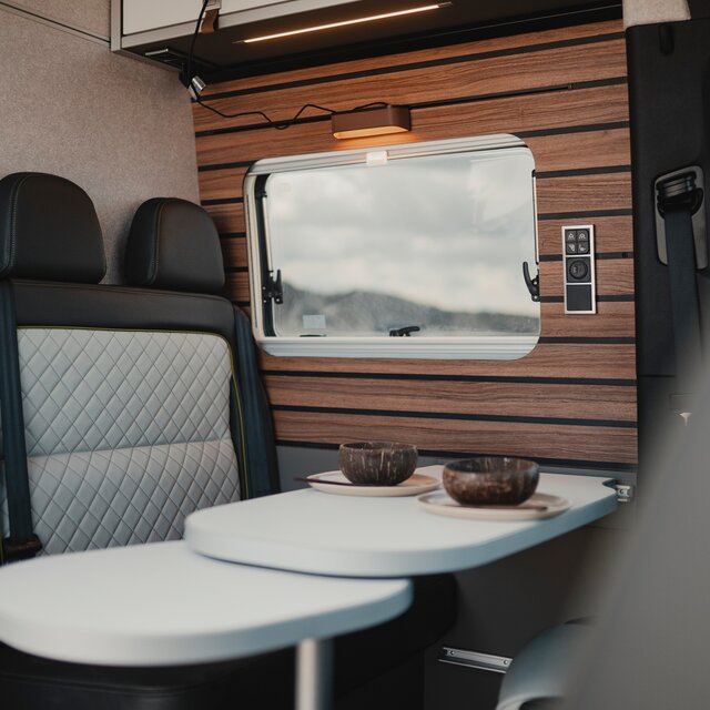 Modern interior in a camper van, seating area with set table, in the background the side window