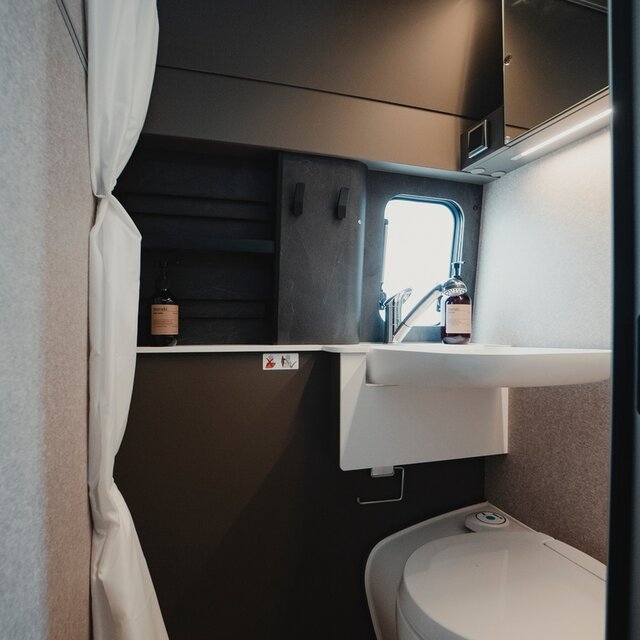 Bathroom in a camper van: shower cabin with sink, cassette toilet, mirror, storage cabinets, shower curtain
