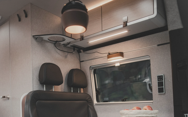 View of the area above a seating group in a campervan, where various light sources can be seen on, under, above, and in front of an overhead storage compartment.