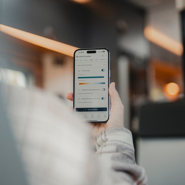 Person using the HYMER Smart Connect app on their phone while sitting in a motorhome
