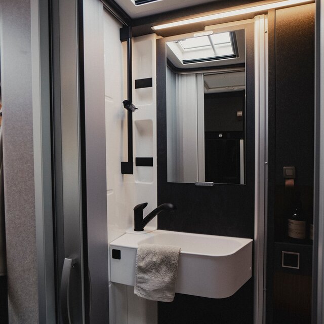 Comfort bathroom in a motorhome: shower cabin with sink, mirror, storage cabinets made of dark wood, shower fixtures
