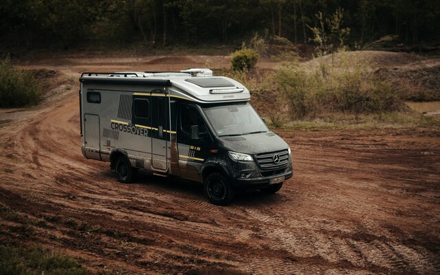 Semi-integrated 4x4 motorhome seen from the front and side, driving through an off-road park and is dirty