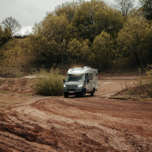 Semi-integrated 4x4 motorhome drives through an off-road park and is dirty, the LED light bar is on