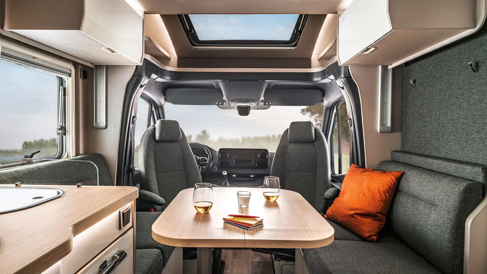 Seating group with laid table and decorative cushions and driver's cab with driver's seats turned into a seating group in the HYMER T-Class S.