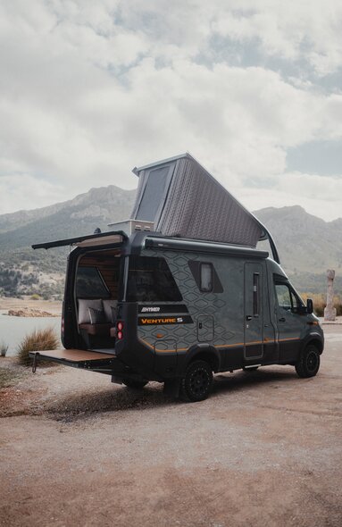 Utsikt fra bakre side av Venture S, med taket og Sunset Deck utfoldet, med fjell og vann i bakgrunnen.